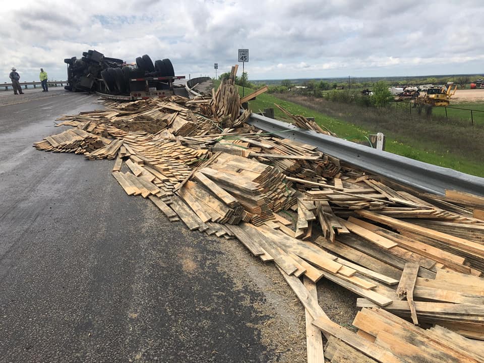 Overturned semi-trailer with spilled lumber cargo on a Central Texas highway, first responders on scene