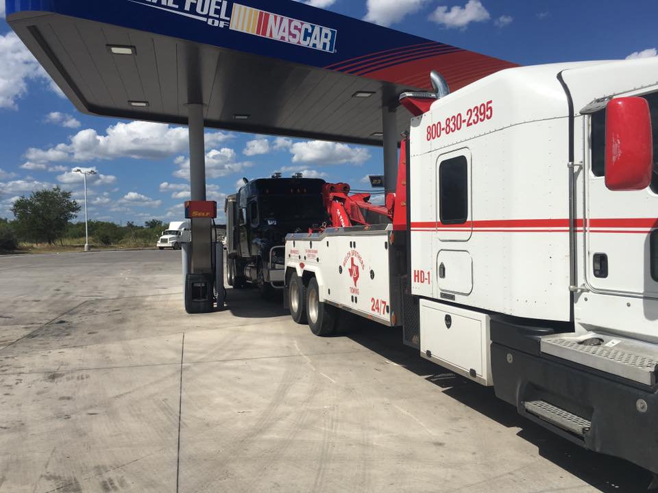 Welch Bros Towing heavy-duty wrecker towing a commercial truck at a highway fuel station